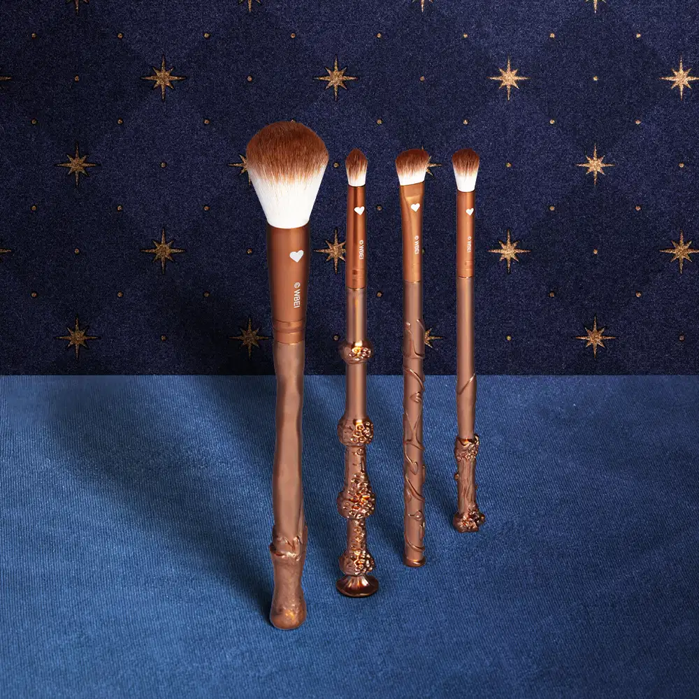 Kit de 4 pincéis de maquiagem com design inspirado na marca Harry Potter, em tons dourados e pretos, com detalhes decorativos em formato de varinha mágica. Eles estão em superfície azul e fundo verde com estrelas douradas.