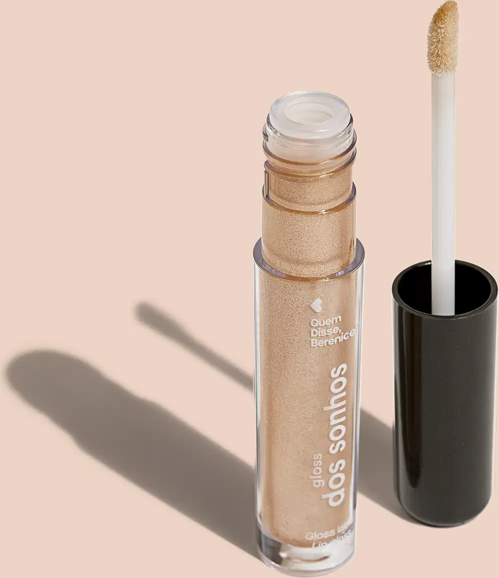 Frasco cilíndrico transparente contendo um brilho labial dourado brilhante. Rótulo na embalagem com o nome do produto "Gloss dos Sonhos" e a descrição "Quem disse, berence?". Ao lado, a tampa preta do produto, que acompanha um aplicador.
