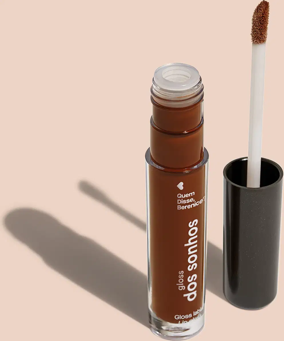 Frasco cilíndrico transparente contendo um gloss labial marrom. Rótulo na embalagem com o nome do produto "Gloss dos Sonhos" e a descrição "Quem disse, berence?". Ao lado, a tampa preta do produto, que acompanha um aplicador de espuma.