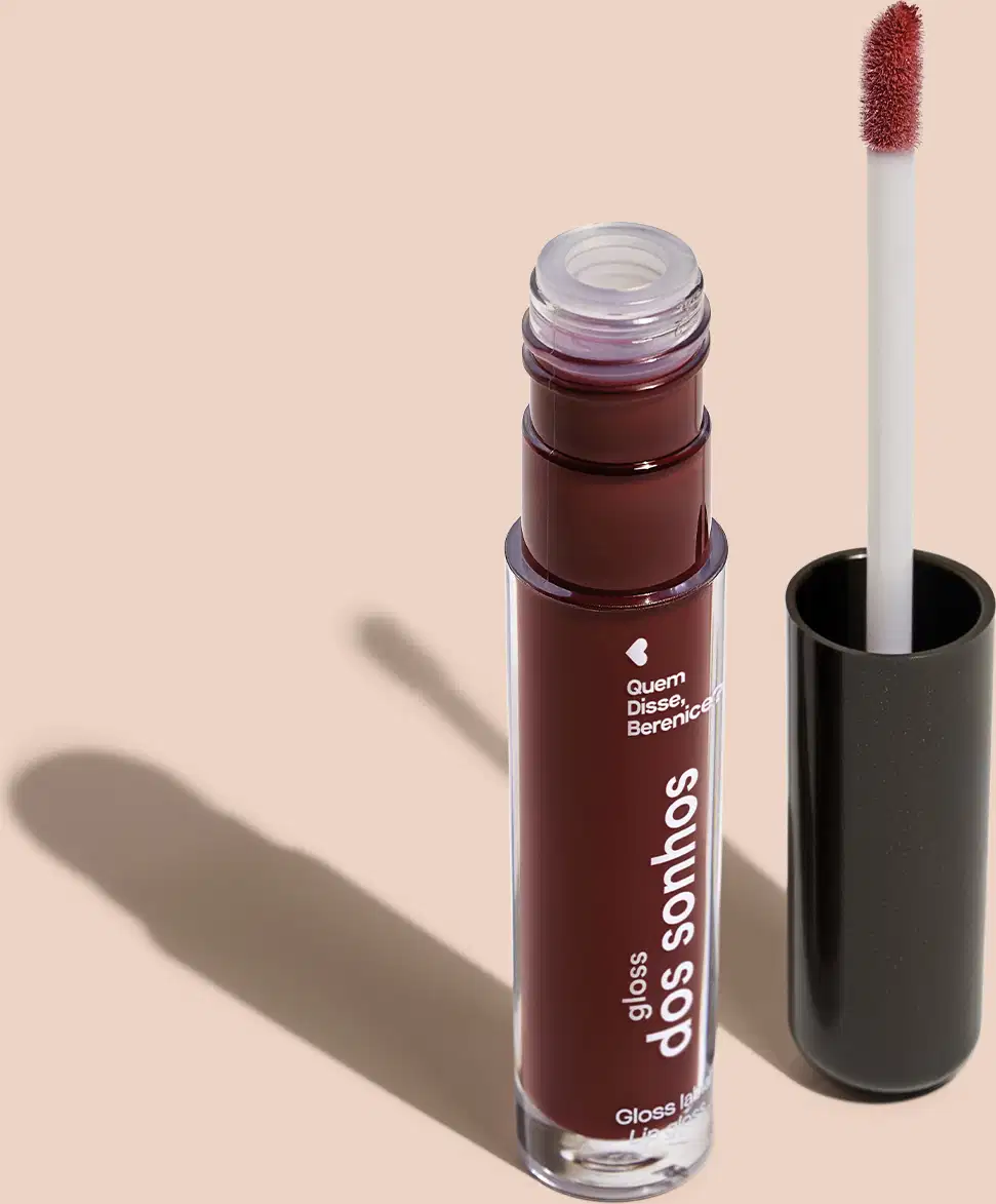 Frasco cilíndrico transparente contendo um gloss labial roxo. Rótulo na embalagem com o nome do produto "Gloss dos Sonhos" e a descrição "Quem disse, berence?". Ao lado, a tampa preta do produto, que acompanha um aplicador de espuma.