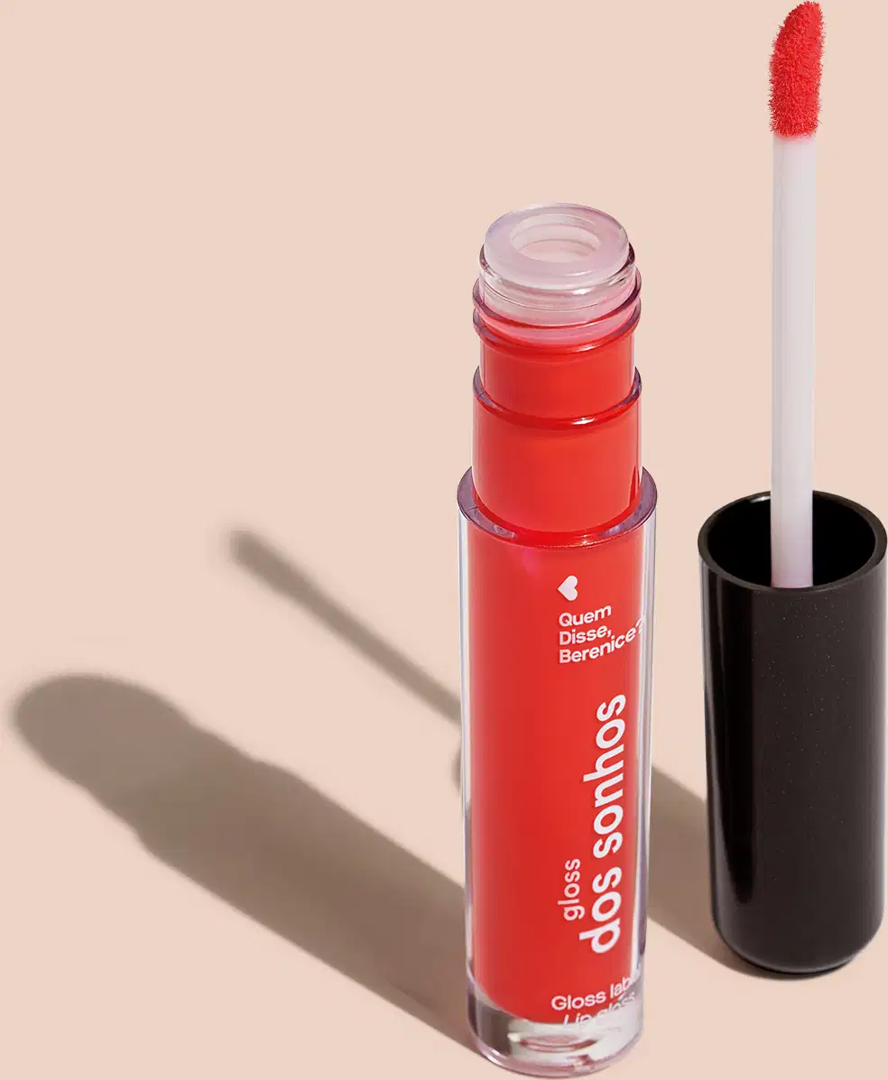 Frasco cilíndrico transparente contendo um gloss labial vermelho. Rótulo na embalagem com o nome do produto "Gloss dos Sonhos" e a descrição "Quem disse, berence?". Ao lado, a tampa preta do produto, que acompanha um aplicador de espuma.