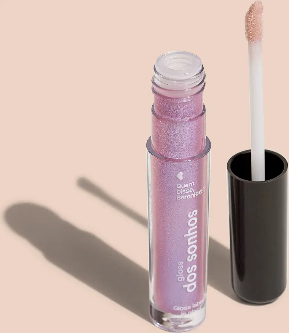 Frasco cilíndrico transparente contendo um gloss labial rosa com púrpura. Rótulo na embalagem com o nome do produto "Gloss dos Sonhos" e a descrição "Quem disse, berenice?". Ao lado, a tampa preta do produto, que acompanha um aplicador de espuma.