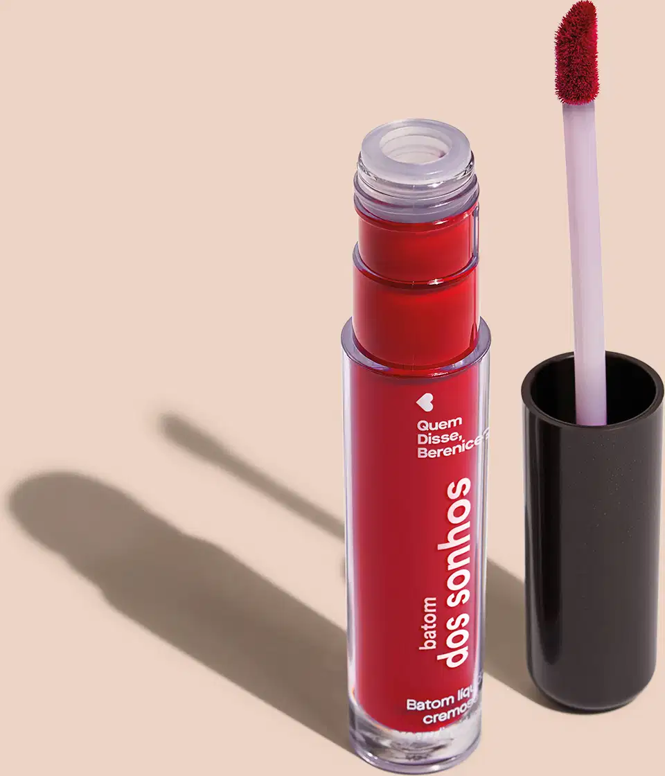 Batom líquido Vermelho em frasco transparente de plástico, com aplicador de espuma. O frasco possui uma tampa protetora preta para guardar o aplicador. O rótulo no frasco exibe o nome da marca e do produto em letras brancas sobre fundo vermelho.