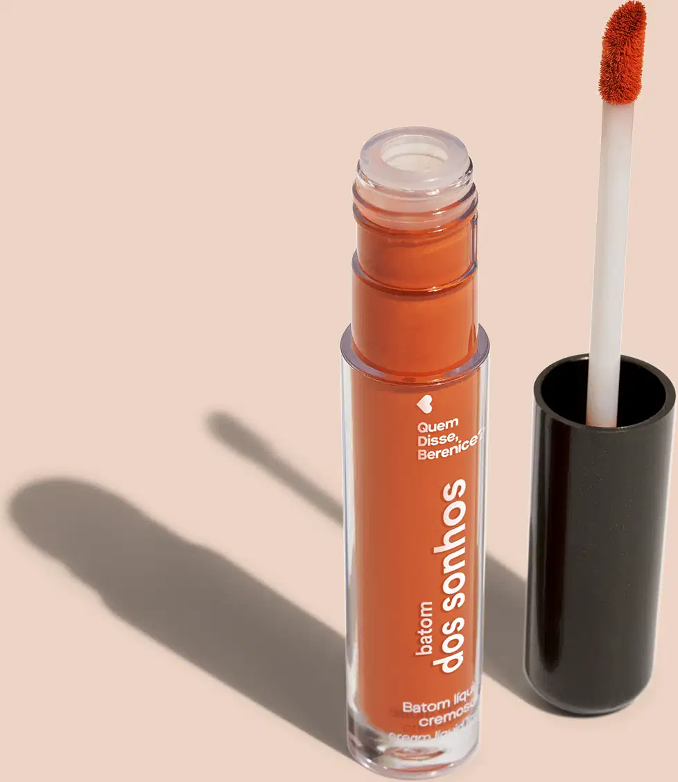Batom líquido Laranja em frasco transparente de plástico, com aplicador de espuma. O frasco possui uma tampa protetora preta para guardar o aplicador. O rótulo no frasco exibe o nome da marca e do produto em letras brancas sobre fundo laranja.