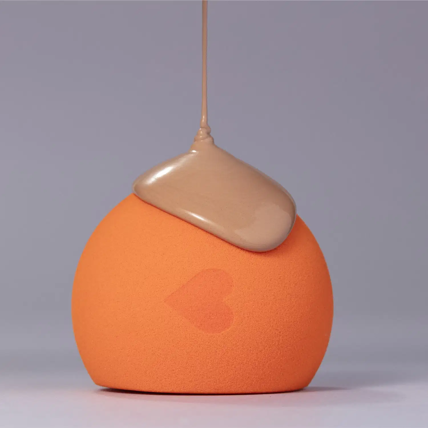 O produto apresentado na imagem é um item de maquiagem da marca Quem Disse, Berenice?. Trata-se de um recipiente com formato arredondado e textura aveludada na cor laranja, com um aplicador em tom bege na parte superior.