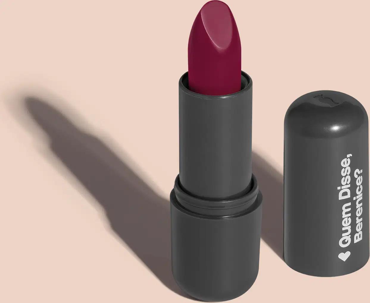Batom de cor pink em embalagem preta com logotipo da marca Quem Disse, Berenice? em destaque. O batom está aberto sobre superfície rosa com iluminação que cria uma longa sombra projetada atrás da embalagem.