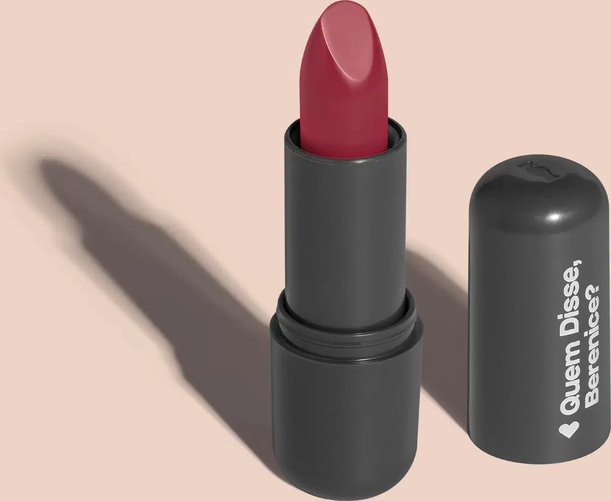 O produto apresentado na imagem é um batom da marca Quem Disse, Berenice?. O batom possui uma embalagem preta com o logotipo da marca em branco. O próprio batom é de uma cor rosa, com um acabamento brilhante.