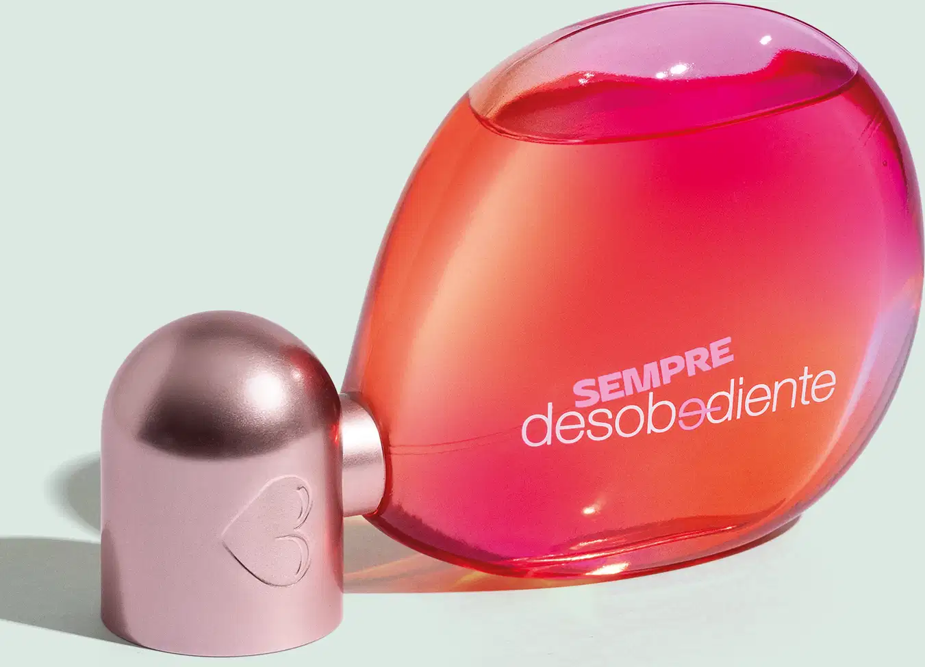 Fragrância em frasco de vidro. O frasco é vermelho alaranjado translúcido. Na parte frontal do frasco está impresso em letras brancas "sempre desobediente". O design é minimalista e moderno, com linhas suaves e formas curvilíneas.