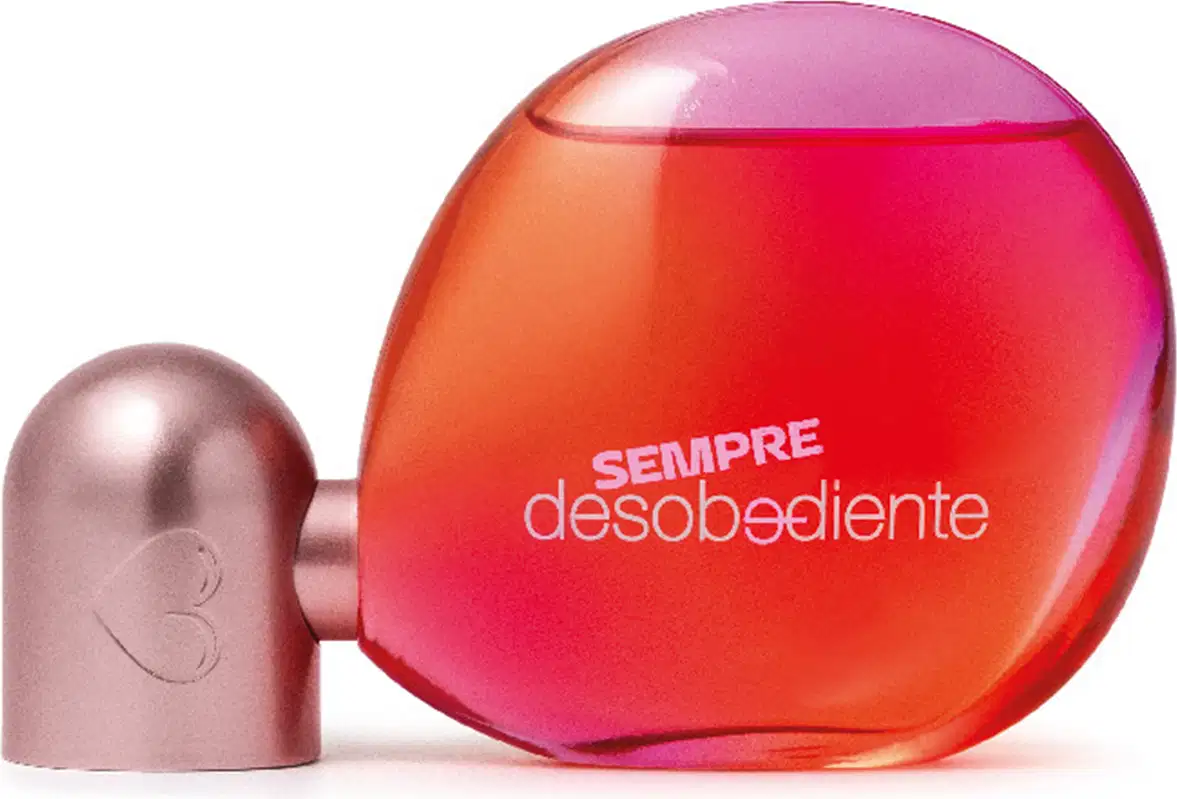 Fragrância em frasco arredondado com tampa em formato de gota. O frasco é translúcido com gradiente de cores que vão do rosa ao laranja vibrante. A tampa é de um tom rosado metálico.