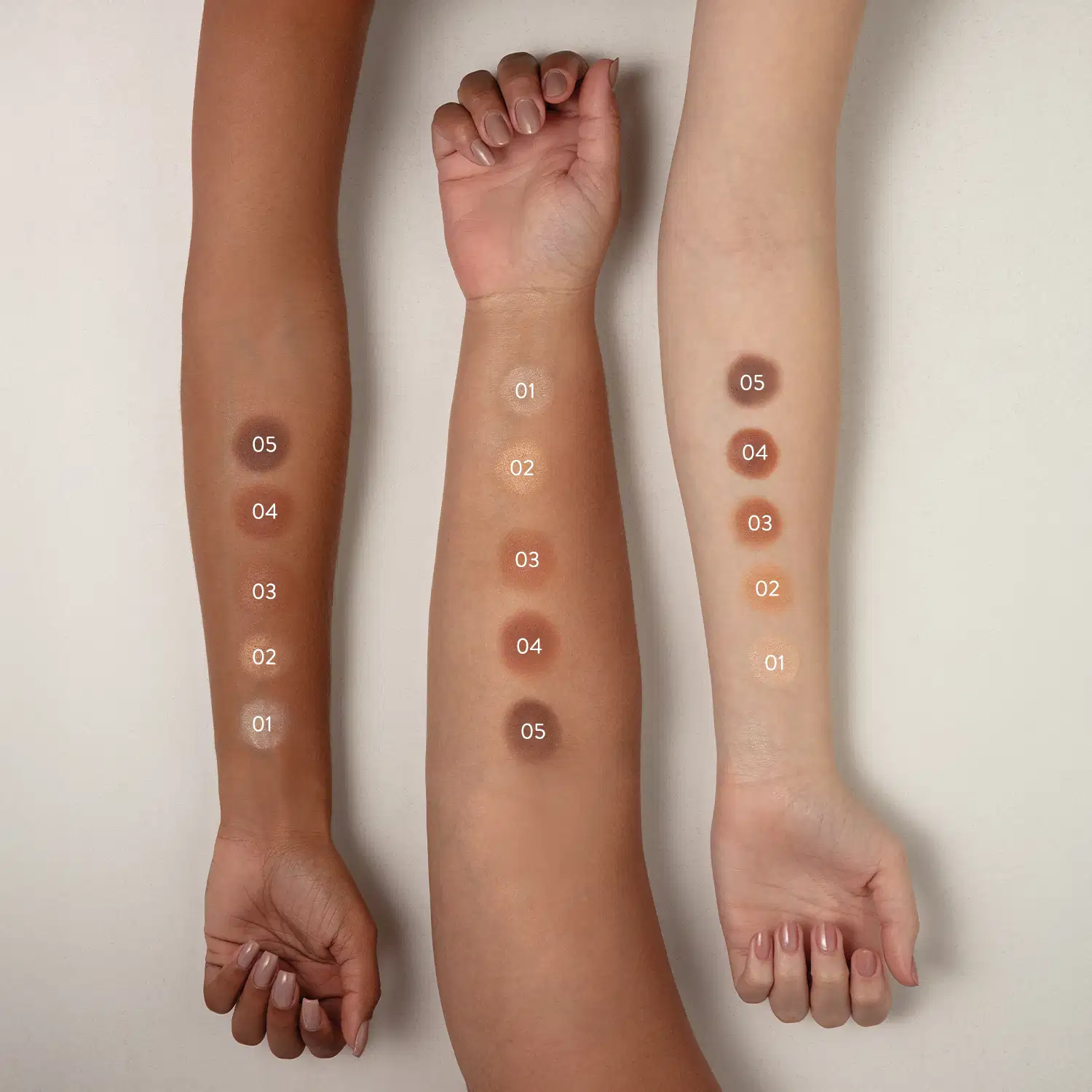 Imagem mostra três braços de cores diferentes estendidos sobre superfície branca sendo o braço mais a esquerda de pele negra, o do meio de pele parda e o da direita com pele branca, todos com diversos tons de pó solto aplicados sobre eles e seus códigos.