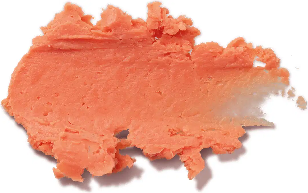 Textura cremosa e densa de tom laranja claro, com superfície irregular e ondulada, espalhada sobre fundo branco, ocupando boa parte da imagem.