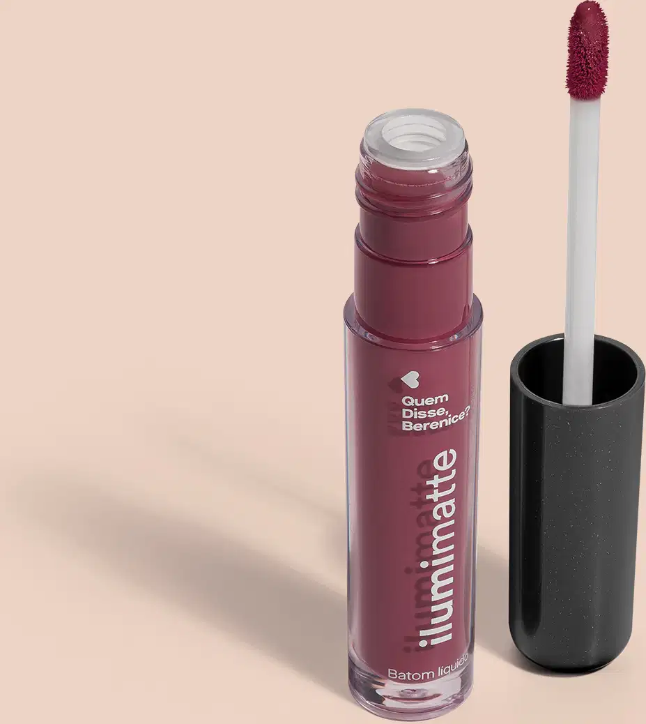 Frasco de batom líquido malva Malvalumi Ilumimatte Quem Disse, Berenice? aberto, mostrando a tonalidade do produto,, com a tampa preta ao lado que traz haste branca e esponja aplicadora na cor rosa escuro em fundo rosado com leve sombreado.