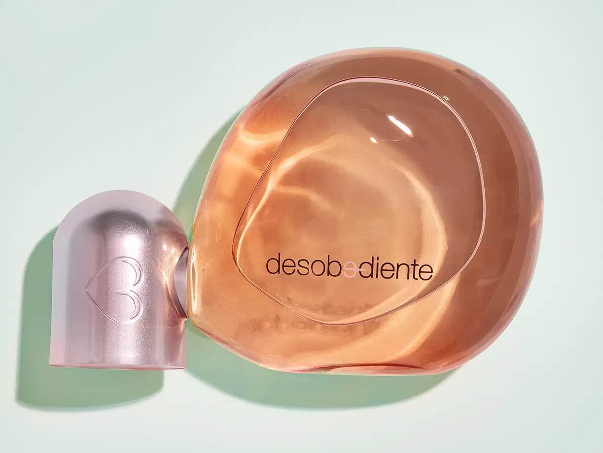 Frasco com líquido rosa e detalhes rose gold contendo 100ml de Eau de Parfum Desobediente Quem Disse, Berenice? em fundo azul claro.