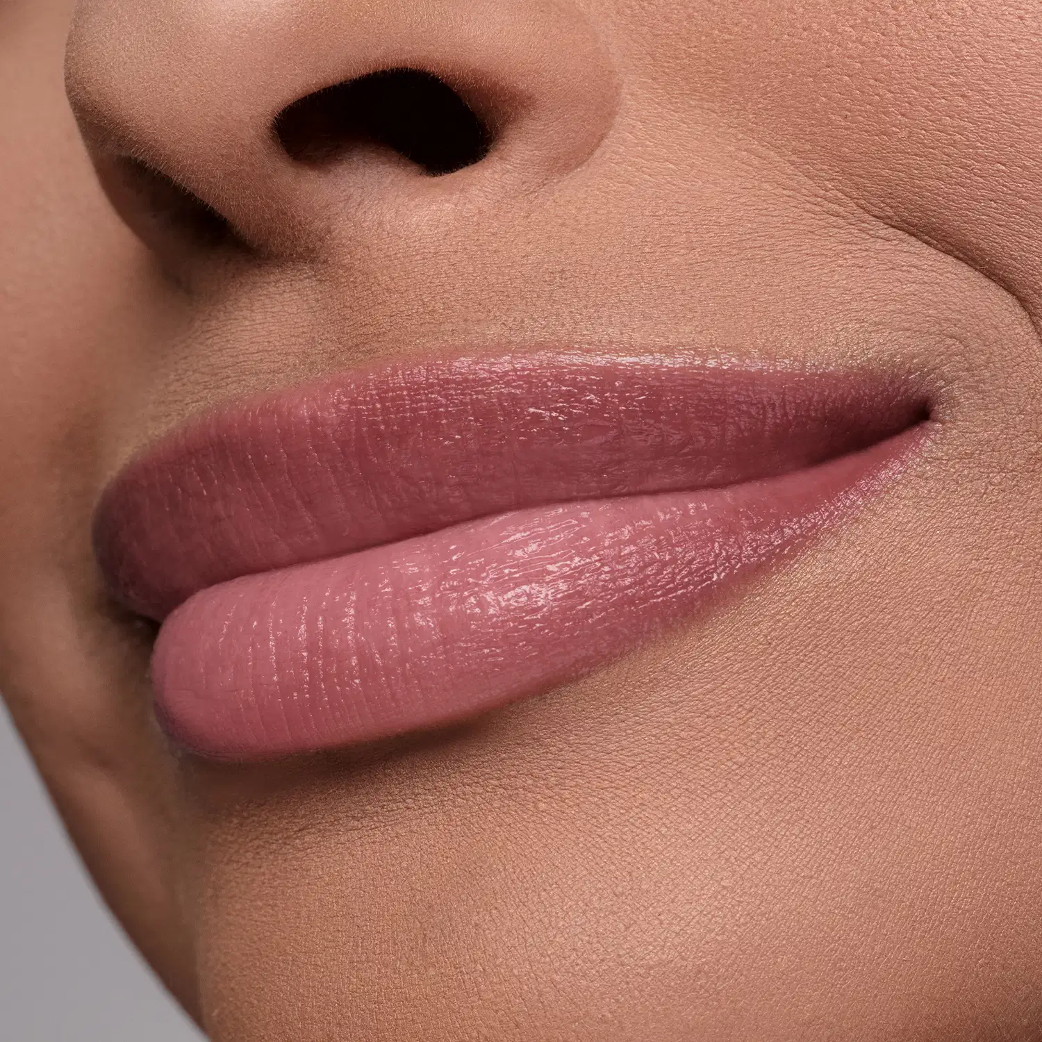 Lábios rosados em primeiro plano, com textura brilhante e suave, sugerindo se tratar do balm labial Melancia Cuide-se Bem Quem Disse, Berenice? em um ambiente com tons neutros e iluminação natural.