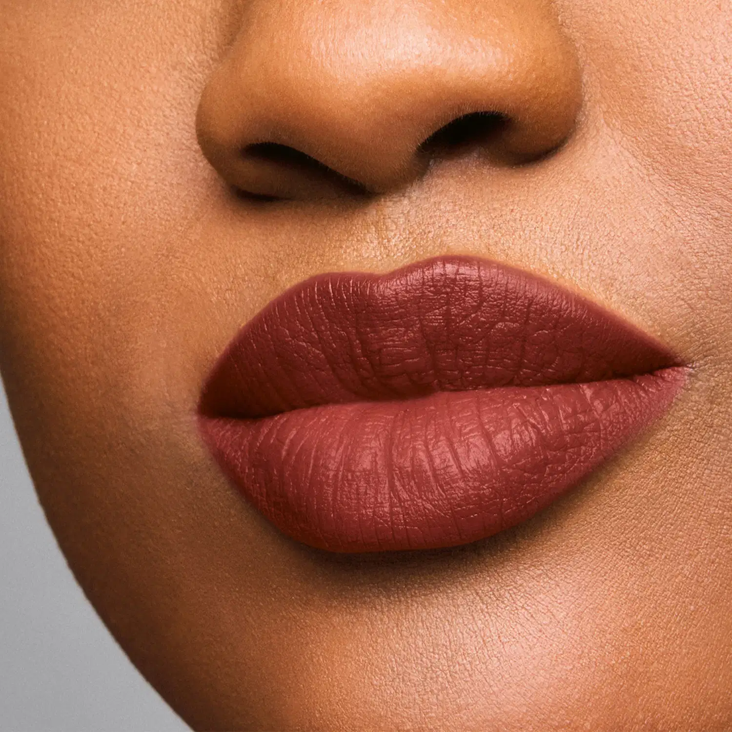 Imagem de um rosto feminino em close-up, evidenciando os lábios com batom cremoso em tonalidade de marrom chocolate.
