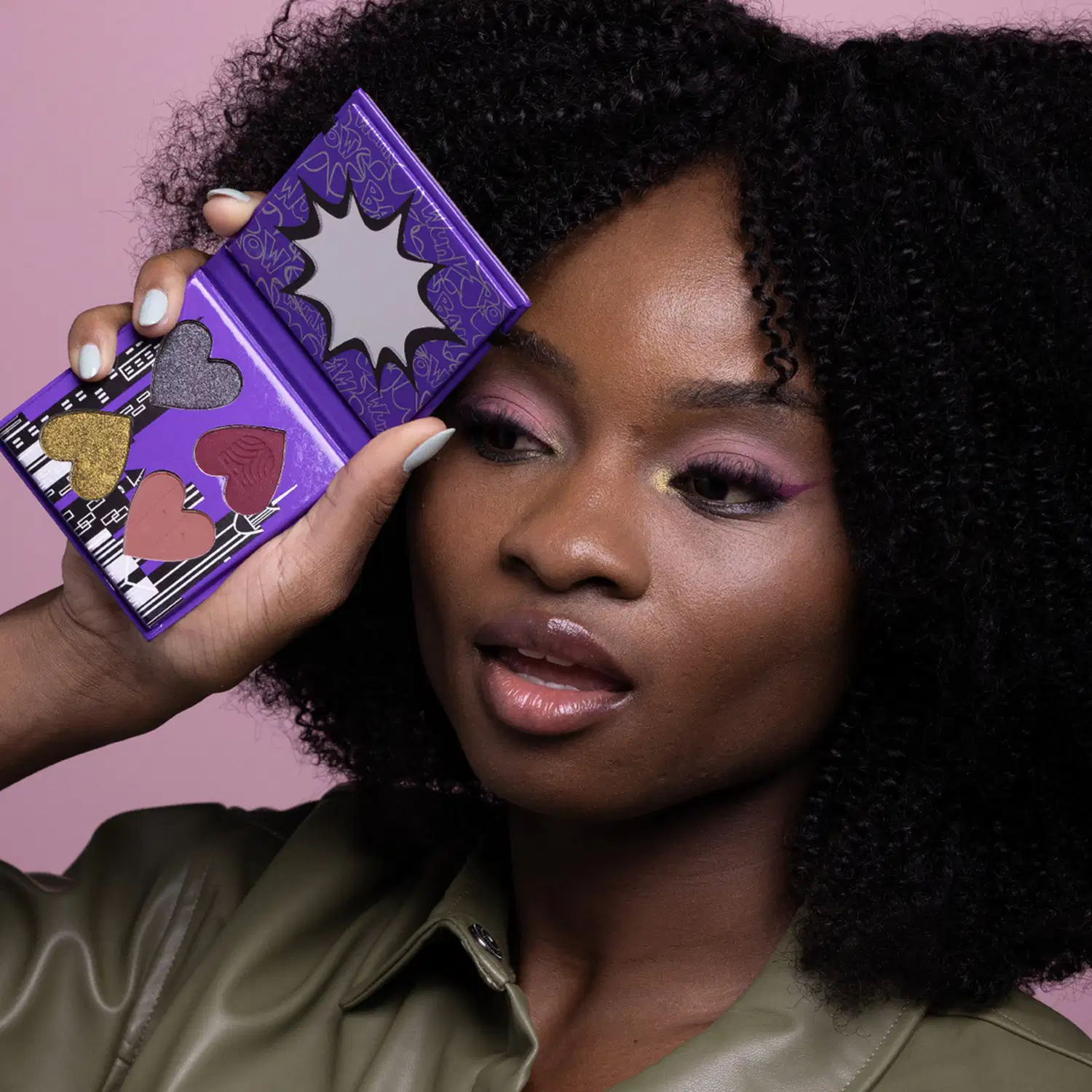Uma mulher de pele negra segura uma mini paleta de maquiagem da marca Meninas Superpoderosas Quem Disse, Berenice? tons de azul e rosa, em um fundo rosa.
