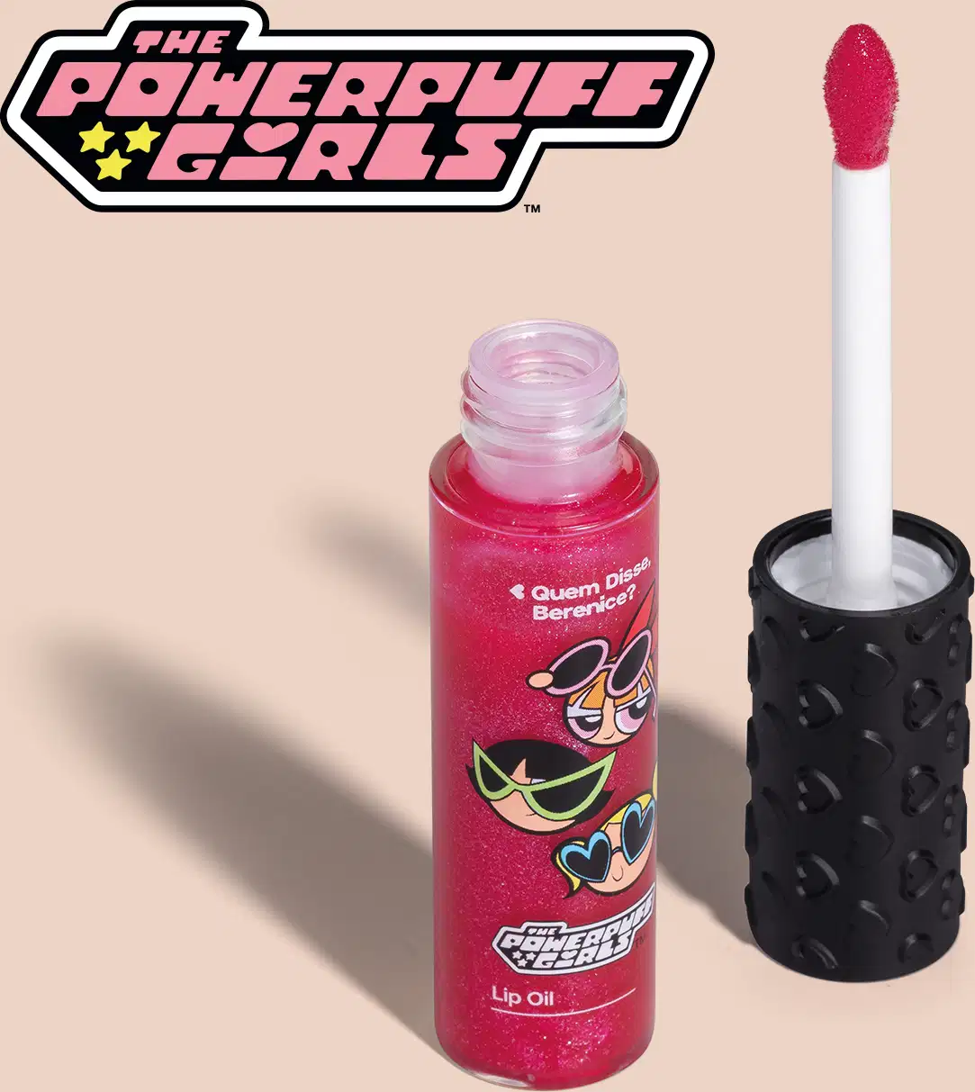 Frasco de lip oil na cor rosa da marca Meninas Superpoderosas Quem Disse, Berenice? em embalagem transparente mostrando a tonalidade do produto, tampa preta com haste e esponjinha vermelha, mostrando ilustração de personagens, em fundo rosa.