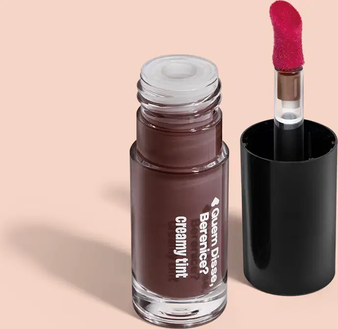 Frasco de vidro contendo um produto de maquiagem em tom marrom escuro, com rótulo indicando "Creamy Tint". Ao lado, um aplicador.