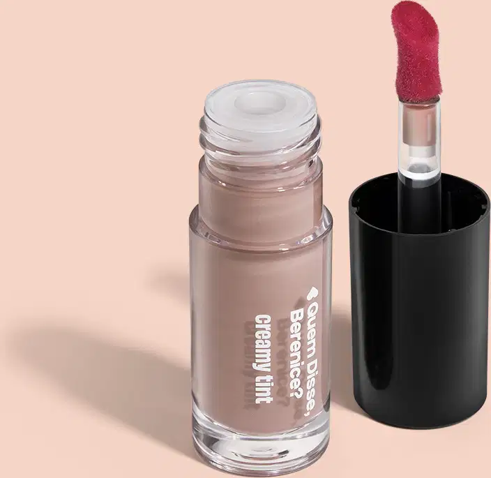 Frasco de vidro transparente contendo um produto de maquiagem em tom rosado, com rótulo indicando "Creamy Tint". Ao lado, um aplicador.