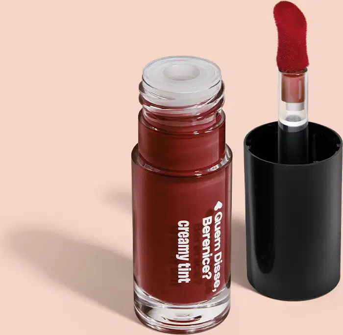 Frasco de vidro contendo um produto de beleza em tom vermelho escuro, com rótulo indicando "Creamy tint". Ao lado, um aplicador.