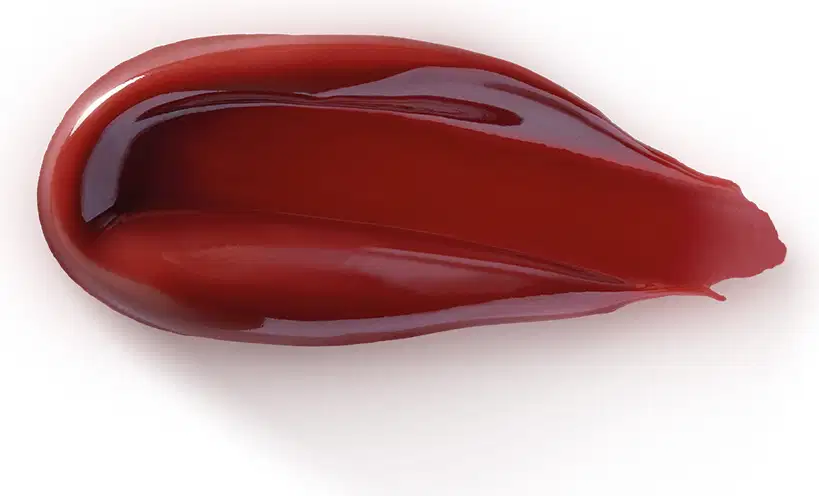 O produto de beleza apresentado na imagem possui uma textura lisa, brilhante e de cor vermelha intensa. Sua aparência é cremosa e viscosa, sugerindo uma consistência densa e untuosa.