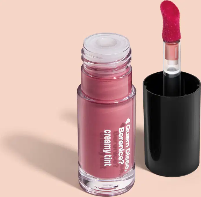 Frasco contendo um produto de maquiagem em tom rosado, provavelmente um batom. O frasco possui um rótulo com o texto "Quem Disse, Berenice?", e o aplicador do produto é visível em sua tampa preta.