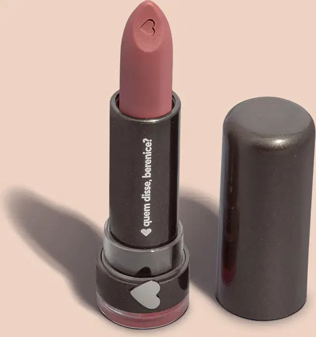 Um item de perfumaria em embalagem preta com logotipo em forma de coração. O produto é um batom de cor rosa escuro com acabamento fosco. O rótulo exibe o nome da marca em letras brancas.