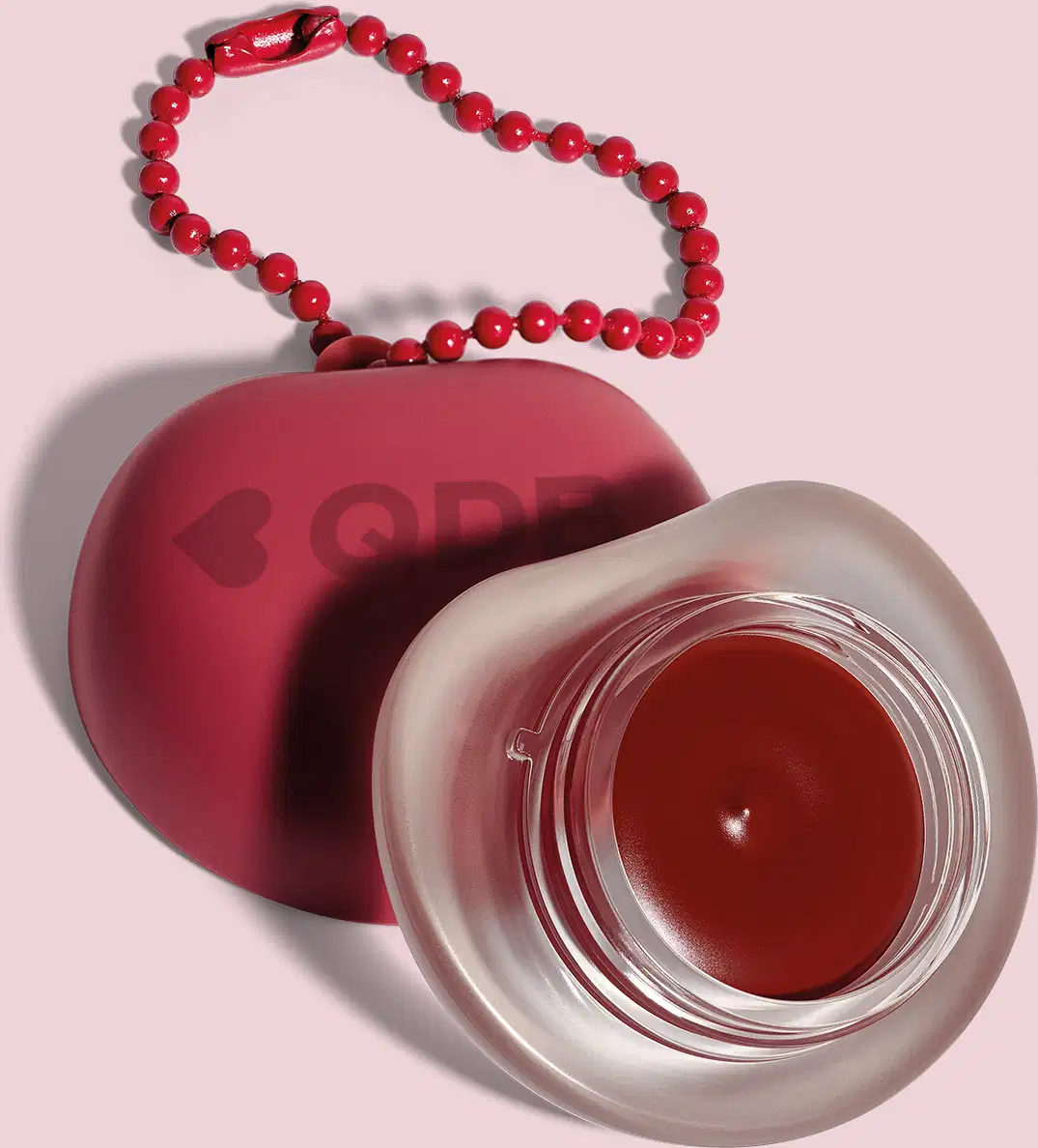 Recipiente vermelho com logotipo em forma de coração, O recipiente está sobre um fundo rosa. A imagem sugere um ambiente relacionado a produtos de beleza e cuidados pessoais.