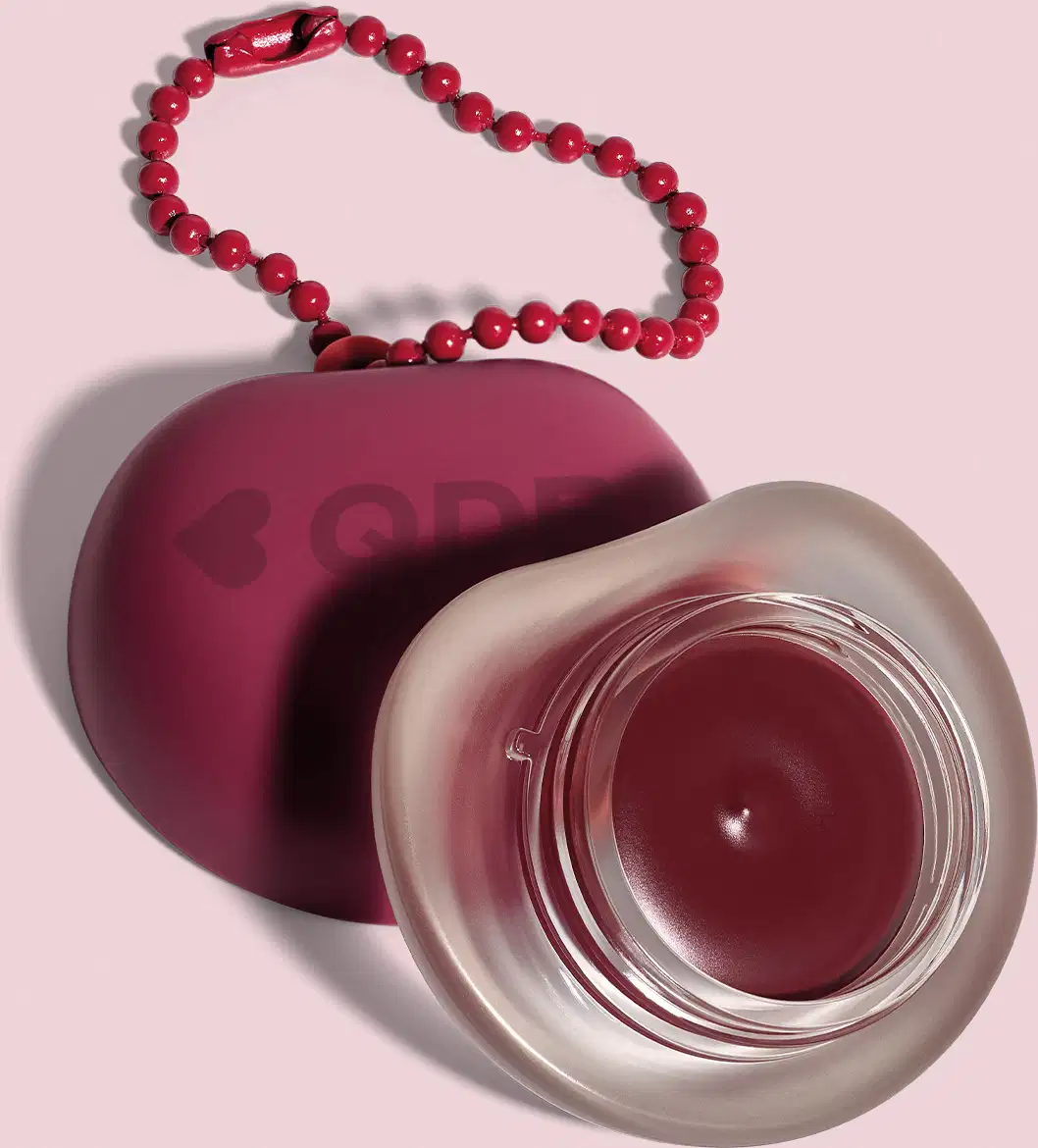Recipiente roxo com logotipo em forma de coração, O recipiente está sobre um fundo rosa. A imagem sugere um ambiente relacionado a produtos de beleza e cuidados pessoais.
