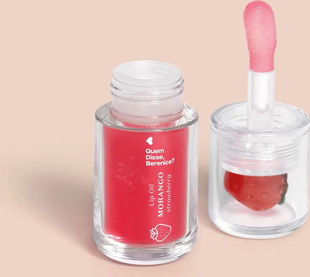 Imagem de um frasco transparente com tampa contendo o Lip Oil Cuide-se Bem Mrango da marca Quem Disse, Berenice. O produto é vermelho e tem aplicador em formato de esponja. Está em um fundo rosa claro com leve sombreado.