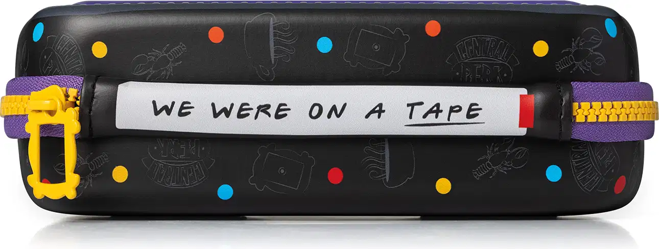 Bolsa preta com estampas coloridas de câmeras, fitas e outros símbolos. Texto "We were on a tape" escrito na parte frontal. Objeto de uso pessoal ou de viagem com design divertido e informal.