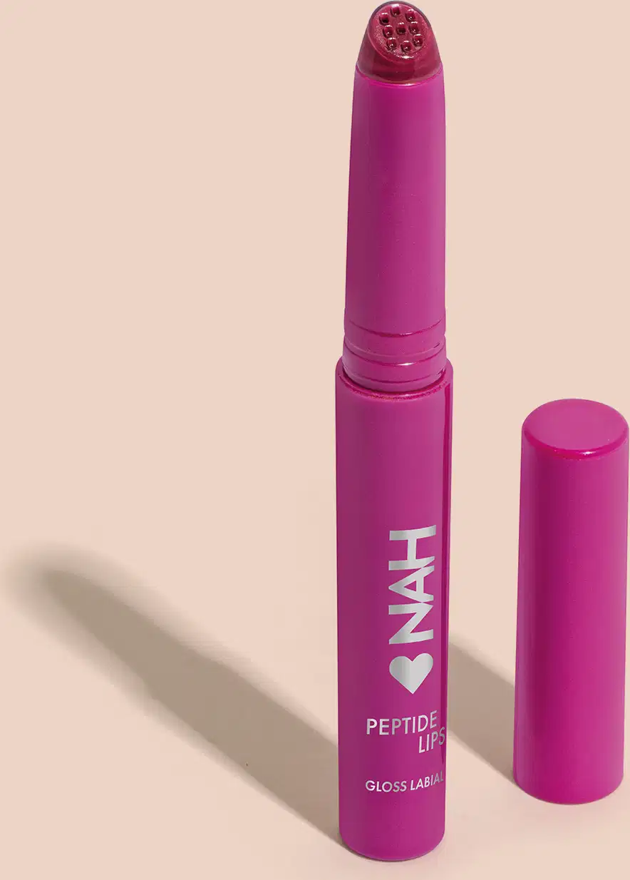 Produto de beleza em embalagem rosa vibrante, com rótulo indicando "Peptide Lips Gloss Labial". Formato de batom, com tampa destacável e corpo cilíndrico.