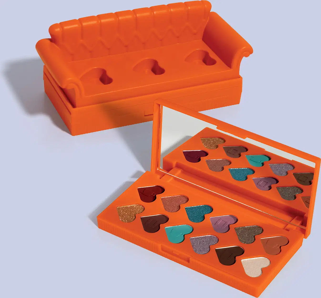 Paleta laranja em forma de sofá com compartimentos em formato de coração, contendo sombras de olho em tons de marrom, dourado e turquesa. A caixa possui uma tampa com encaixes. 
