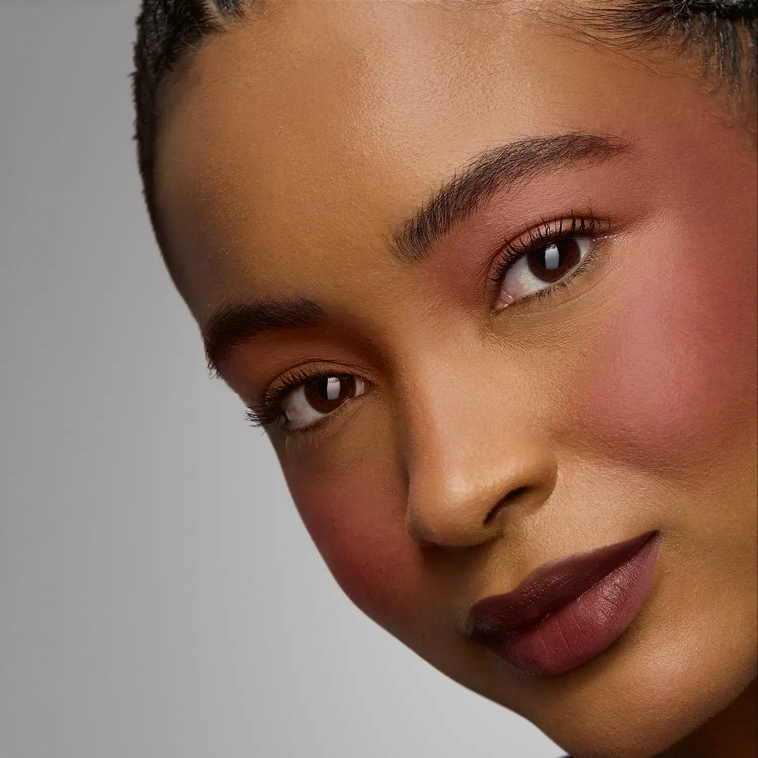 Rosto de uma pessoa com pele negra, olhos expressivos e lábios rosados. Fundo neutro e iluminação suave destacam os traços faciais. A imagem transmite uma sensação de beleza e elegância.