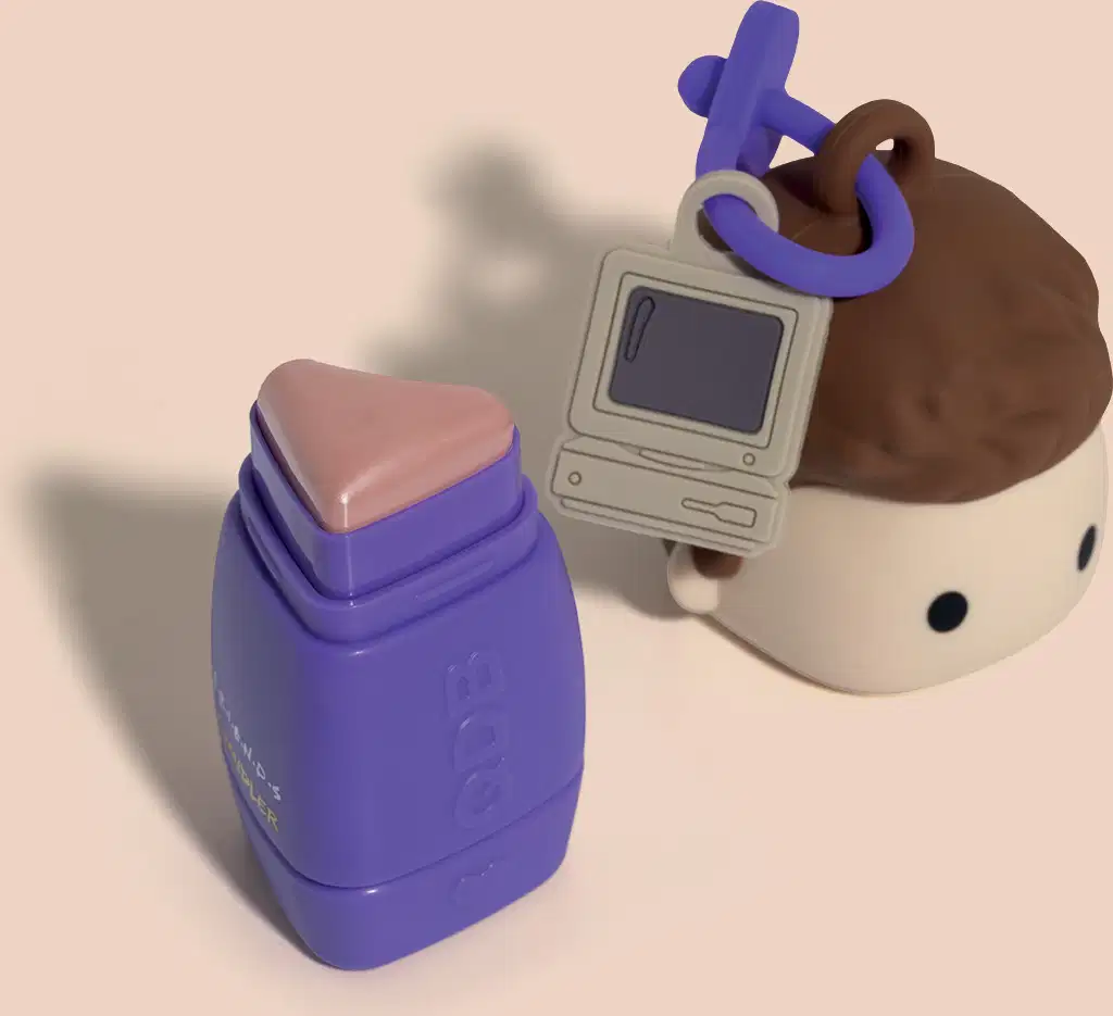 Tampa em formato um boneco com telefone celular e um batom compacto de cor marrom com o texto "FRIENDS CHANDLER" impresso.