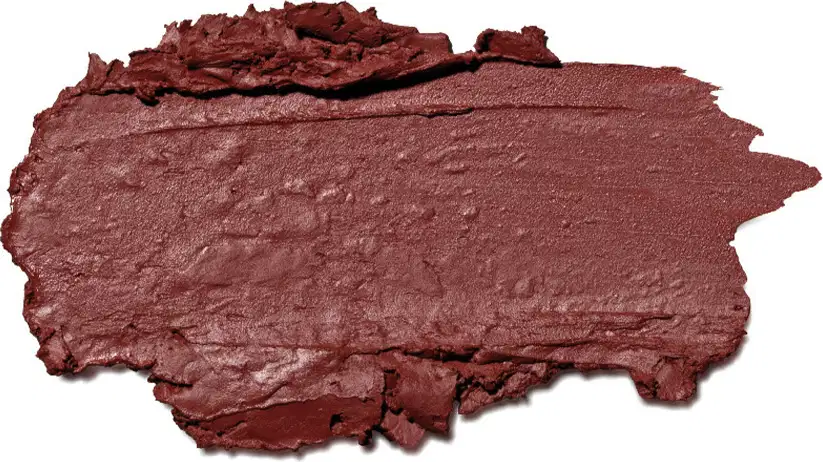 A textura do produto de beleza apresenta uma superfície irregular e áspera, com uma coloração marrom avermelhada predominante. A consistência parece ser cremosa e levemente brilhante, com uma aparência de material compactado.