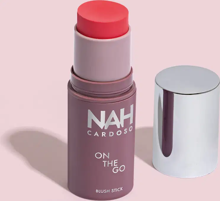 Produto de blush em bastão da marca NAH Cardoso, com embalagem roxa e tampa prateada. O rótulo indica "On the Go" e a cor do blush é rosa.