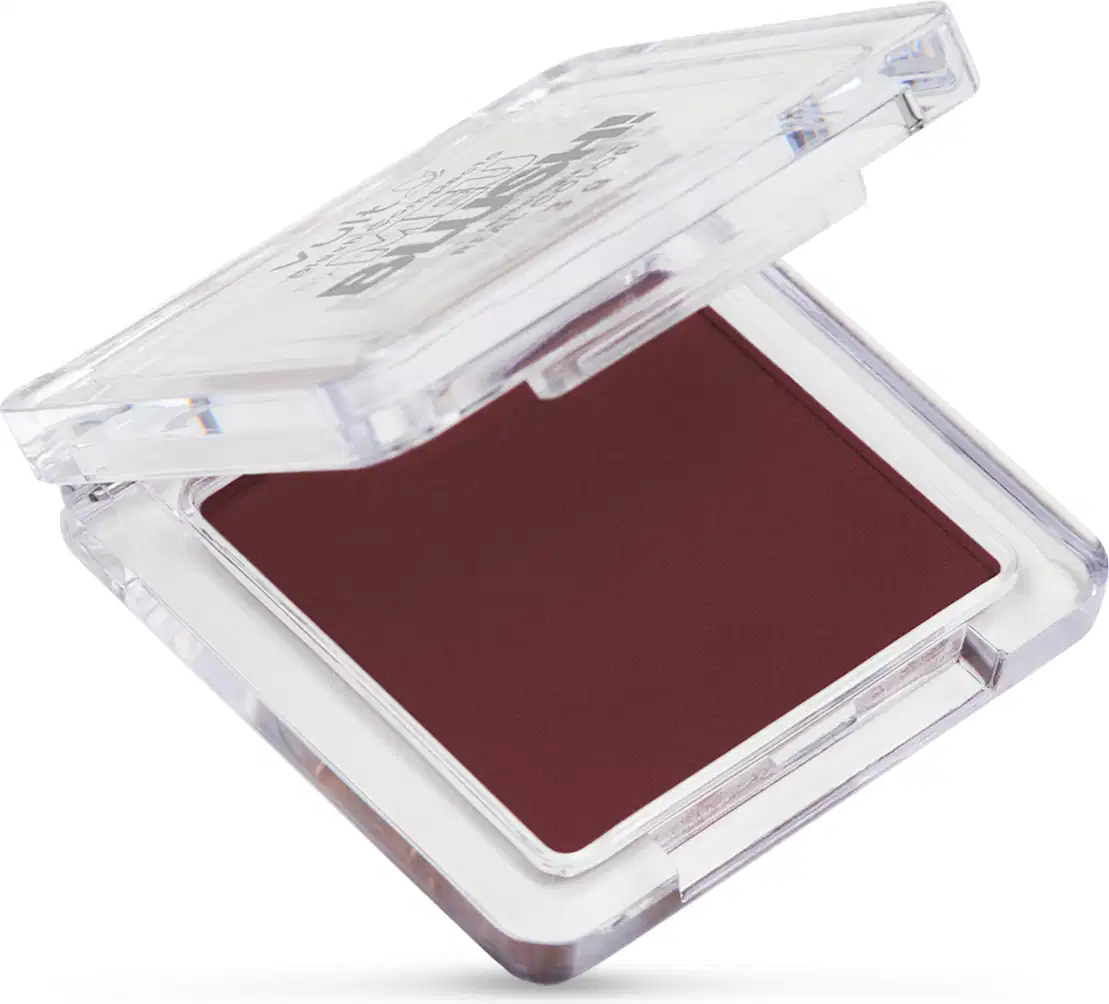 O produto vem em uma embalagem plástica transparente quadrada com tampa articulada. A parte interna contém o pó compacto de cor vinho profundo. A tampa superior tem detalhes gravados com o rótulo. A embalagem permite visualizar a cor do produto.