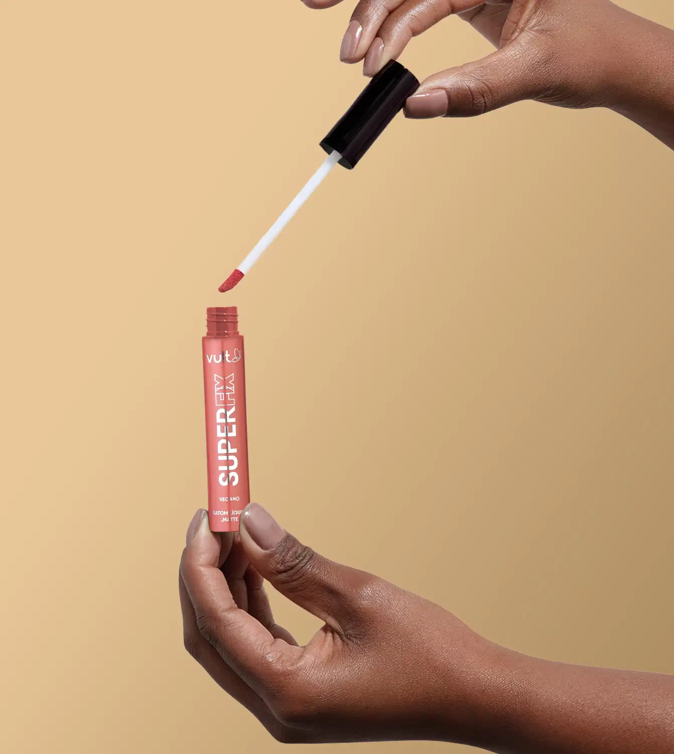 A imagem mostra uma mão segurando o produto aberto do Batom Líquido da marca Vult, na cor castanho. A embalagem do produto é um tubo vermelho com o nome da marca "Vult" impresso.