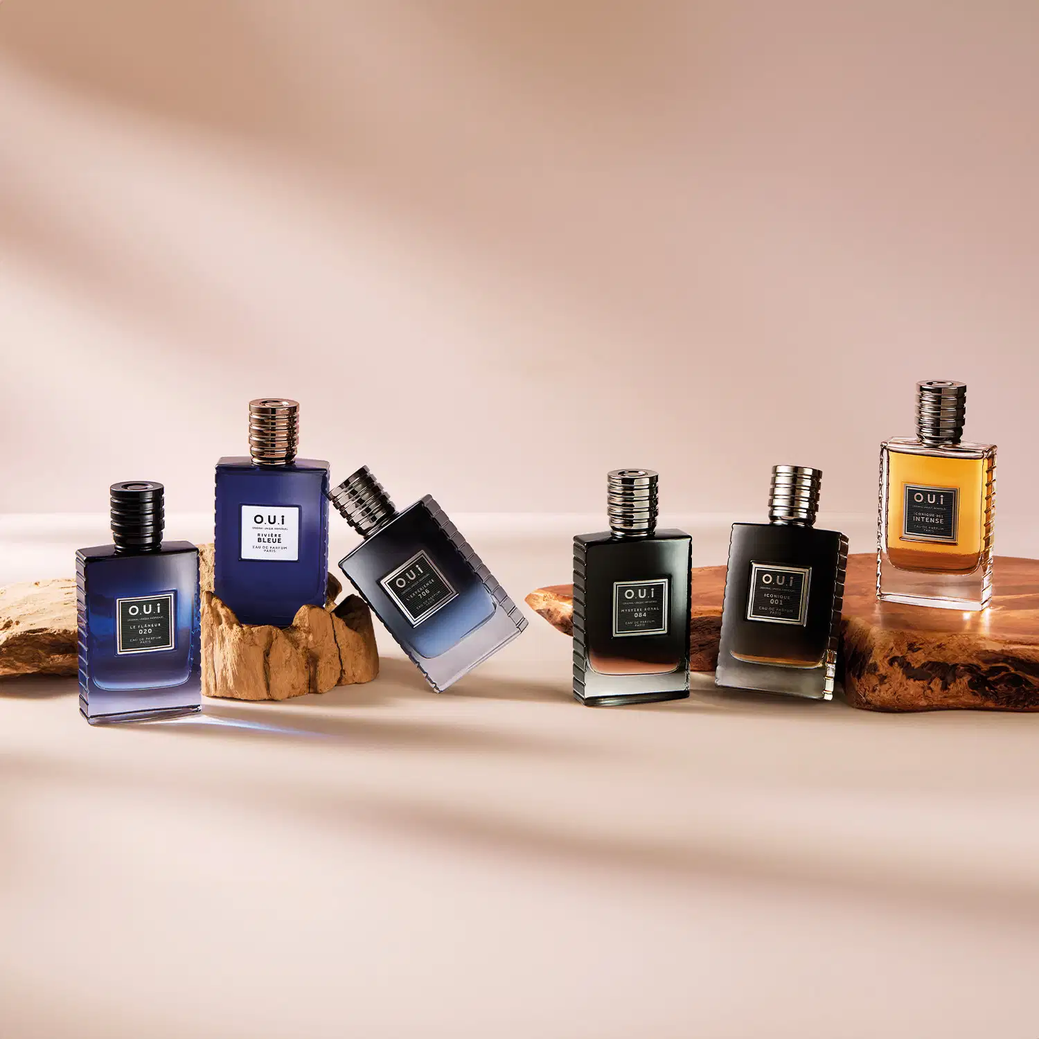 Linha de perfumes da marca O.U.I. Cinco frascos de diferente cores em tons de azul, preto e âmbar. Os frascos têm formatos retangulares e tampas metálicas rosqueadas. O nome da marca "O.U.I" está impresso em letras maiúsculas em cada frasco.