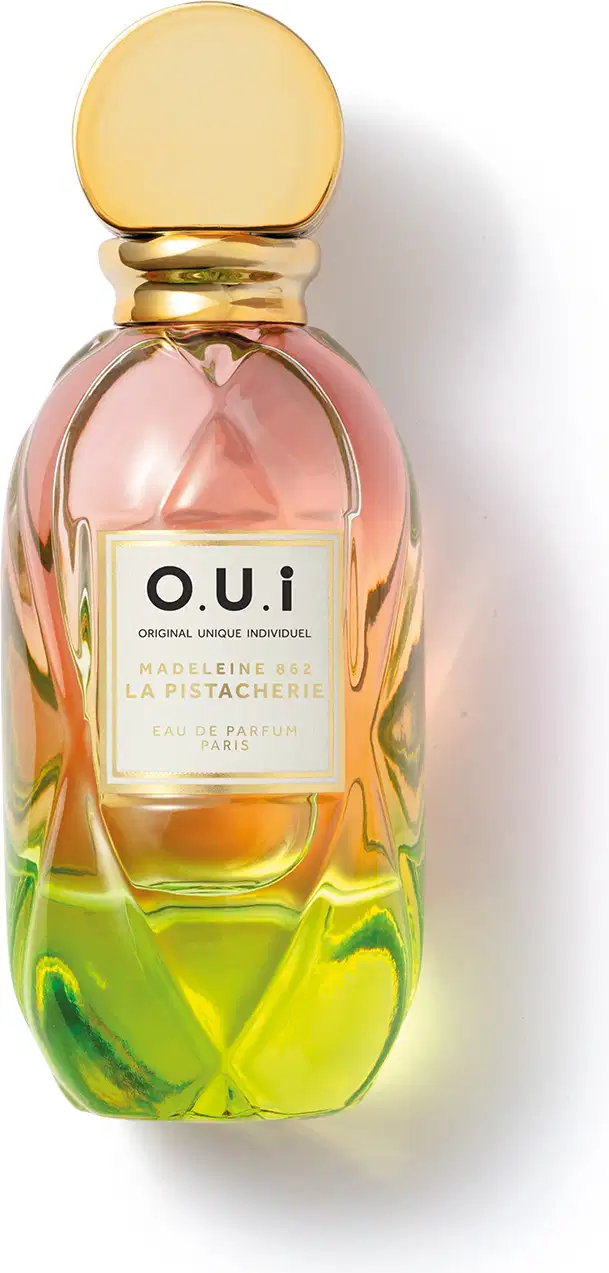 Frasco de perfume O.U.i. com design escultural em tons de rosa, amarelo e verde. Rótulo com nome da marca e informações sobre a fragrância "Madeleine 922 La Pistacherie".