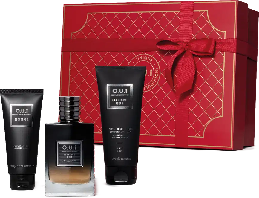 Conjunto. No centro, frasco de vidro contendo líquido da fragrância em degradê de preto à âmbar, de alto a baixo. Ao lado, tubo preto de gel de banho e um tubo preto de creme de barbear. Acompanha caixa vermelha com detalhes em dourado e laço vermelho.