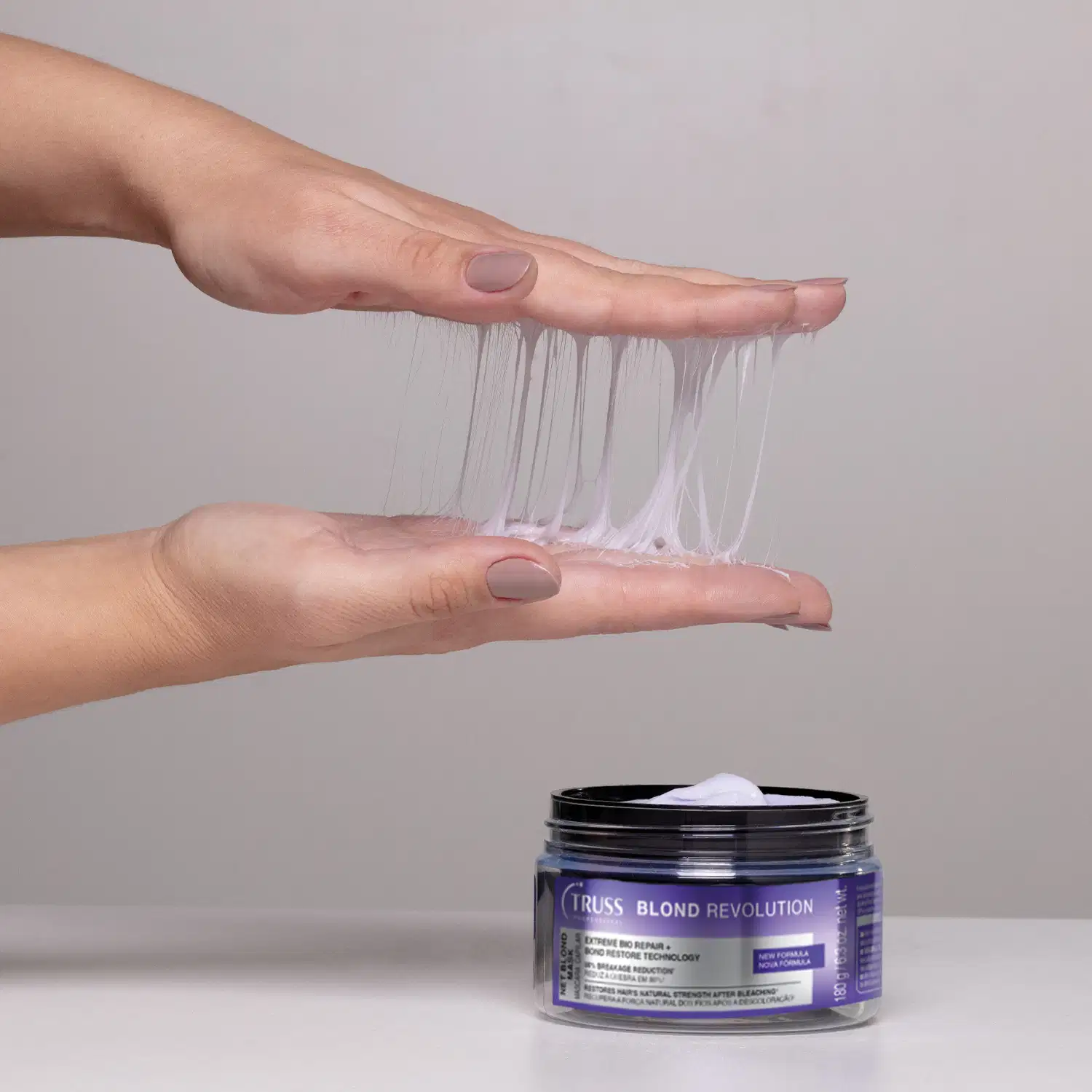 Recipiente preto com rótulo roxo da marca Truss, da Net Mask Blond Revolution. Ao lado, mãos femininas seguram "fios finos" nas mãos, indicando a textura em teia da máscara.