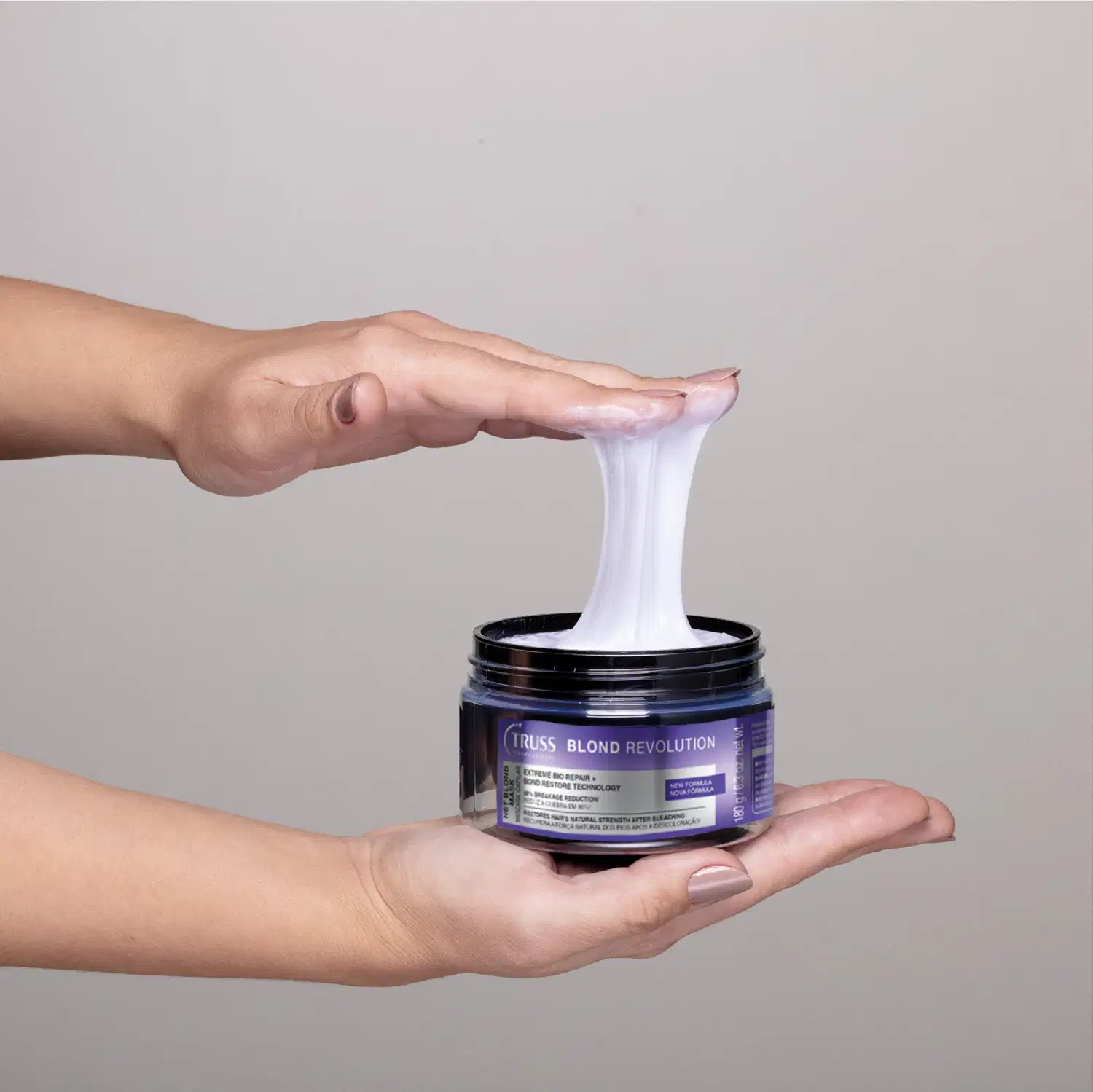 Embalagem preta e branca da Net Mask Blond Revolution. Uma mão segura a parte de baixo do produto, enquanto a outra está em contato com o item, indicando uma textura em teia, cremosa e brilhante.