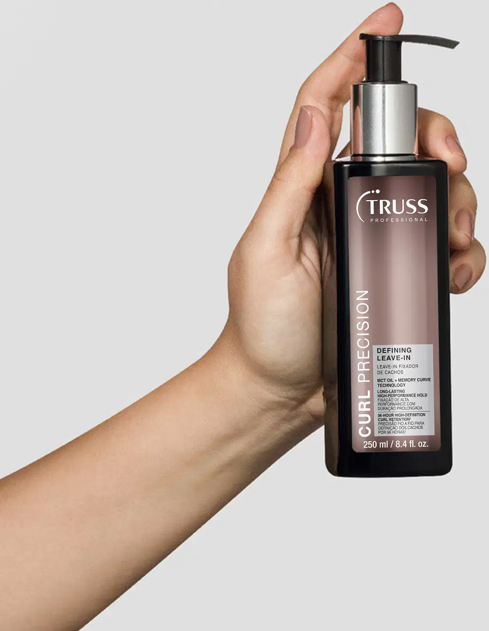 Frasco preto de item de cabelos da marca Truss com bomba doseadora, rótulo com nome "Curl Precision" e texto indicando que é um leave-in finalizador, sendo segurado por uma mão feminina.