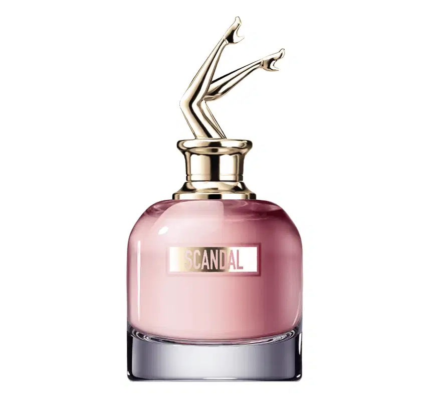Perfume em frasco de vidro rosa com tampa metálica dourada em forma de pernas femininas. O frasco tem base cromada e o rótulo exibe o texto "SCANDAL" em letras maiúsculas douradas.