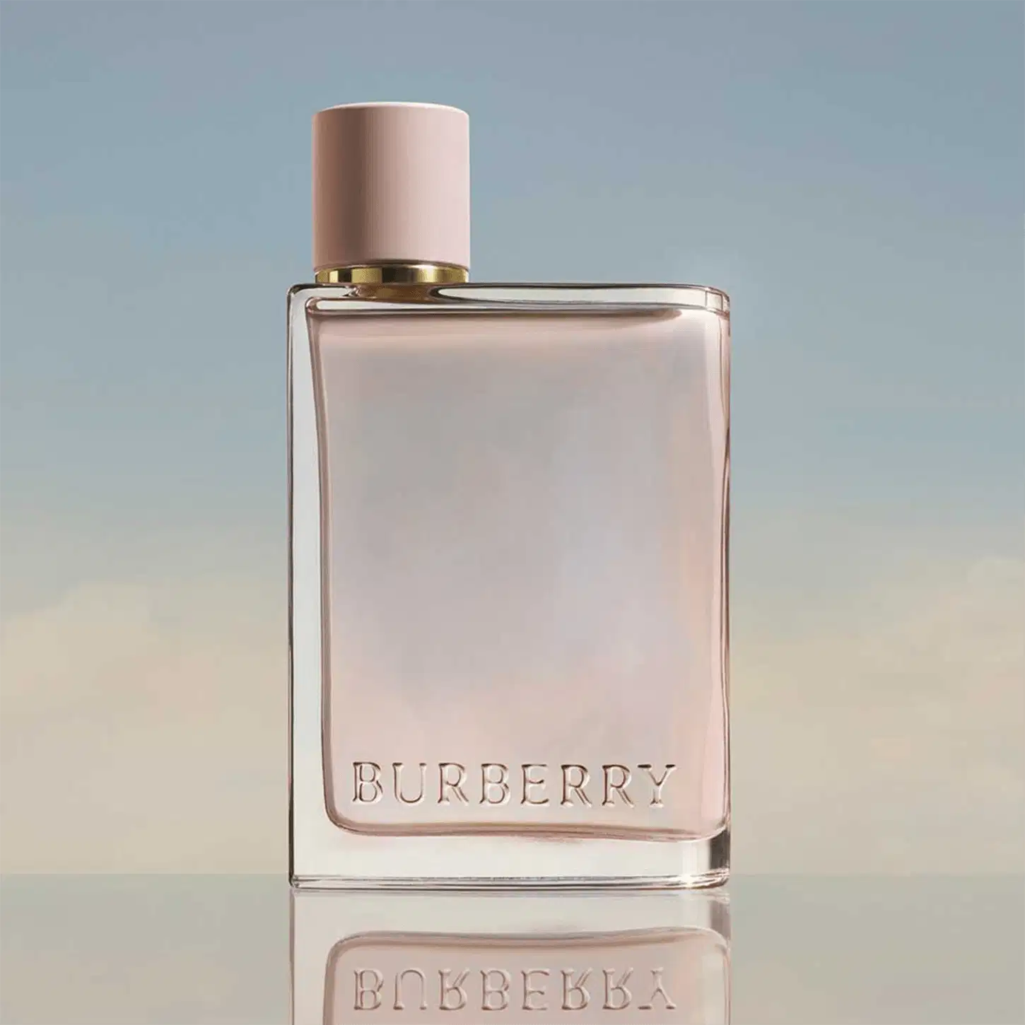 Frasco de perfume Burberry de cor rosa pálido com tampa dourada. O rótulo em destaque exibe o nome da marca "BURBERRY" em letras brancas.