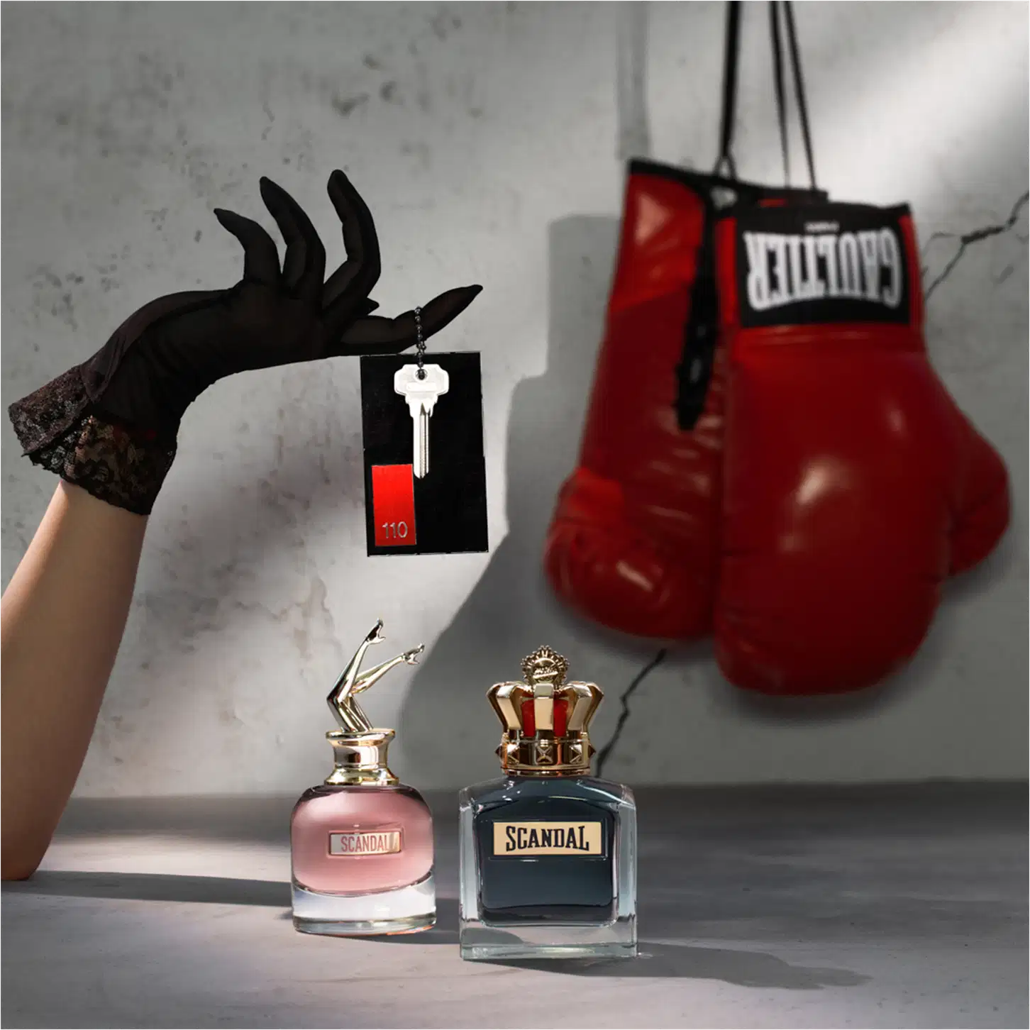 Ambiente de luxo e sofisticação com a marca Scandal da Jean Paul Gaultier. Caixa de presente, luvas pretas e luvas de boxe vermelhas criam um contraste entre elegância e força.