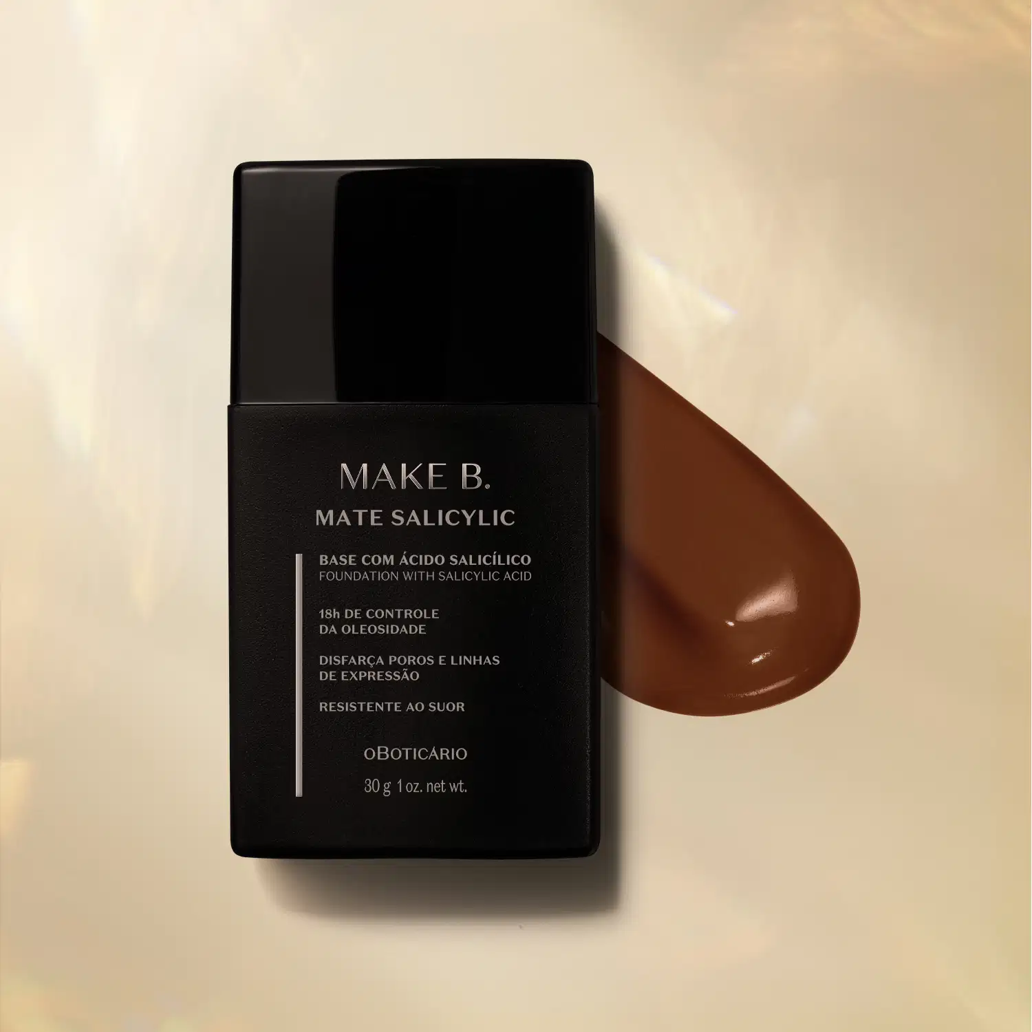 Frasco preto com letras cinzas de base líquida na cor 320 da marca Make B. Mate Salicylic sobre superfície bege com gota de produto marrom escuro ao lado, mostrando textura e tonalidade.