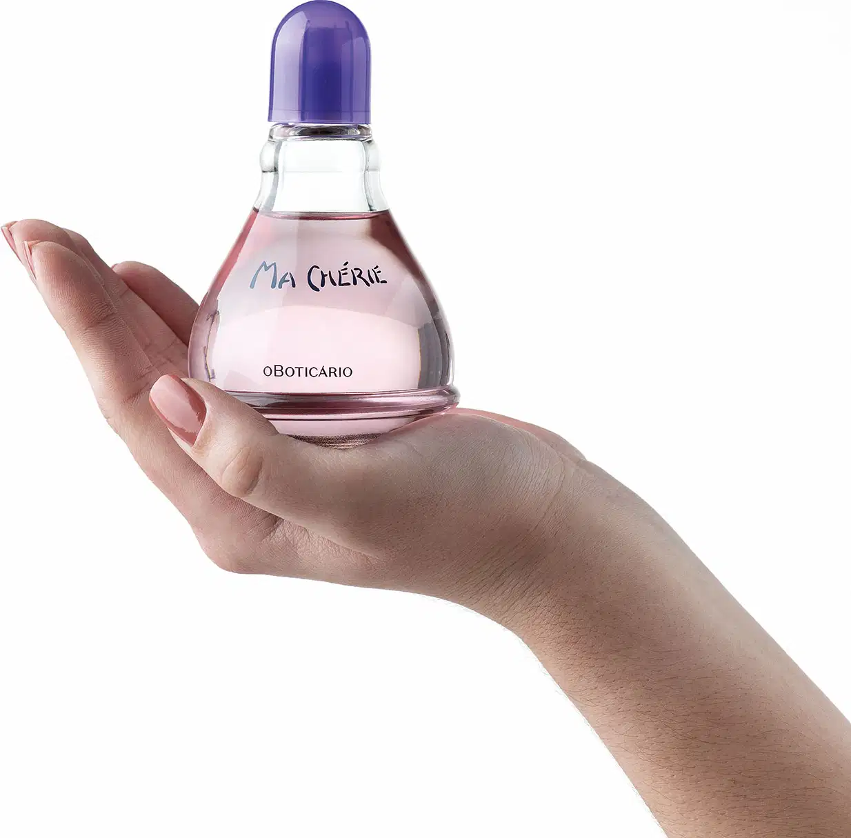 Mão feminina segurando um vidro transparente com fundo arredondado, líquido rosa, tampa e letras azuis, contendo 100ml de desodorante colônia Ma Chérie.